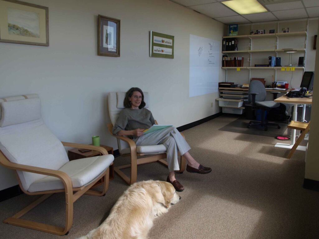 Amy in her office comfy chair with Chinook the office dog in the foreground.